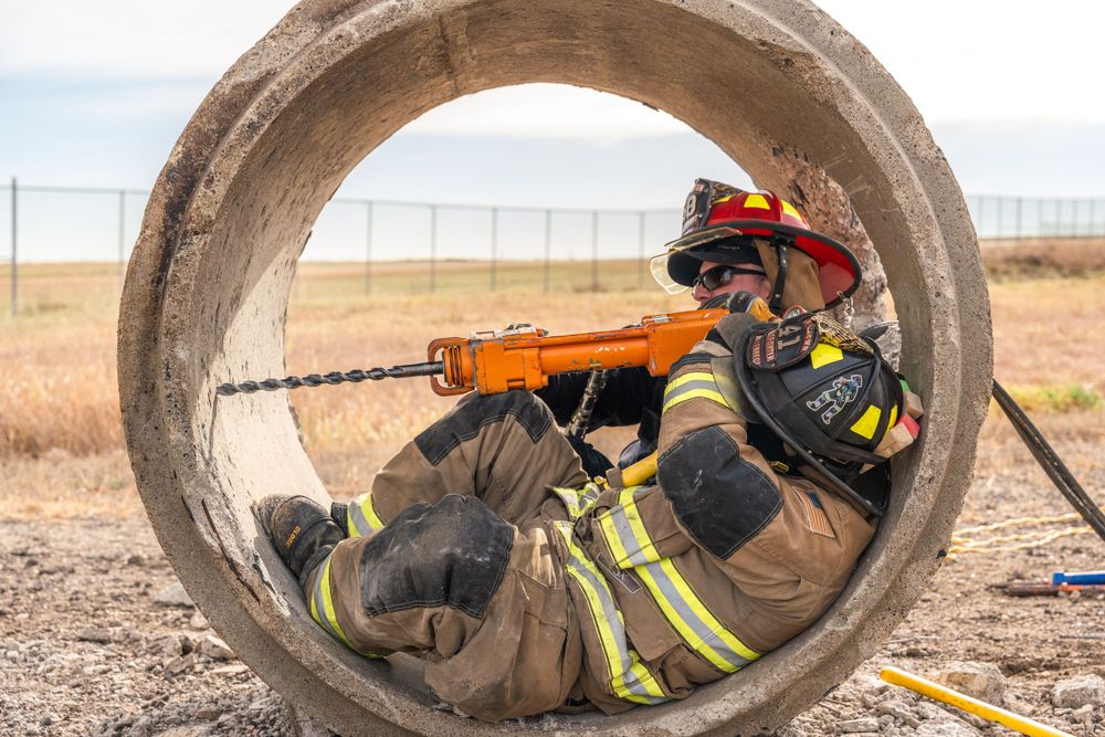 A firefighter in full gear positions inside a large concrete pipe during training exercises at an outdoor facility.