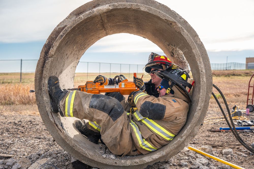 A firefighter in protective gear rests inside a large concrete drainage pipe during training exercises.