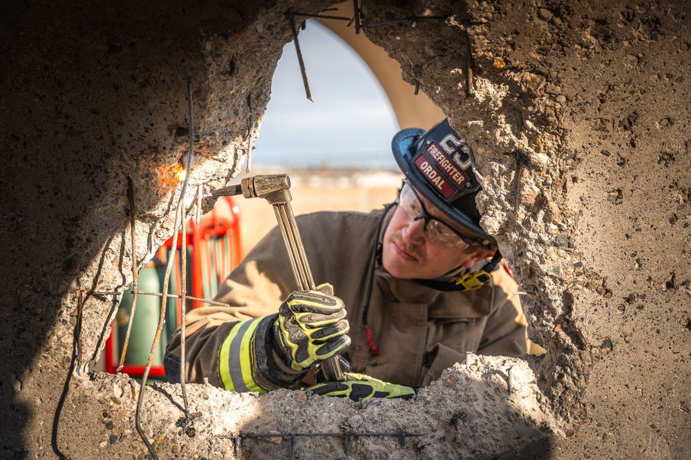 A firefighter peers through a hole in concrete debris during a search and rescue operation.