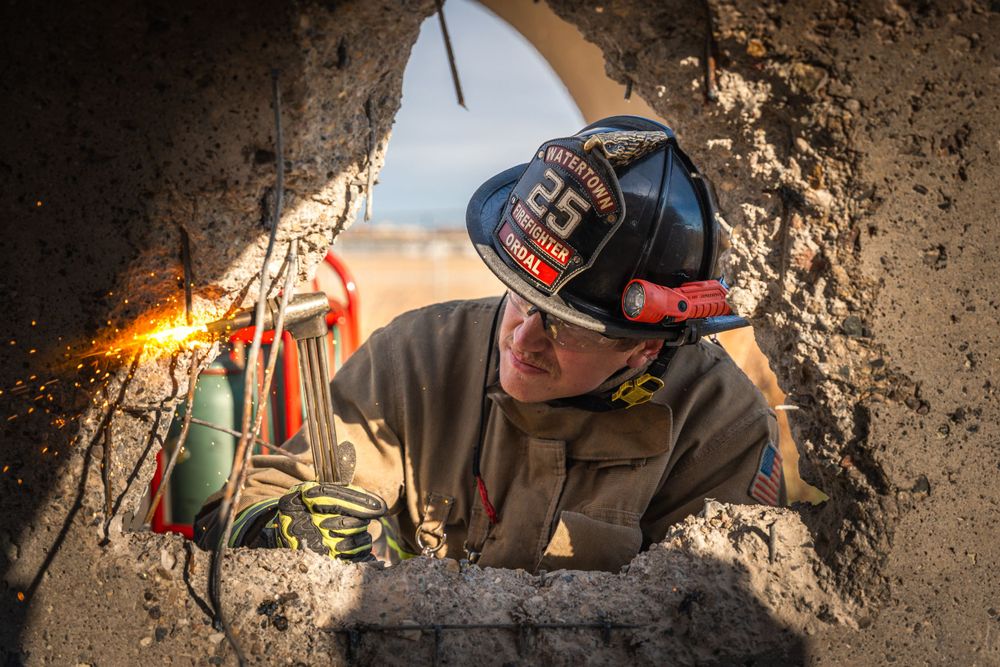 A firefighter works in a confined space during a rescue operation with sunset lighting visible through an opening.