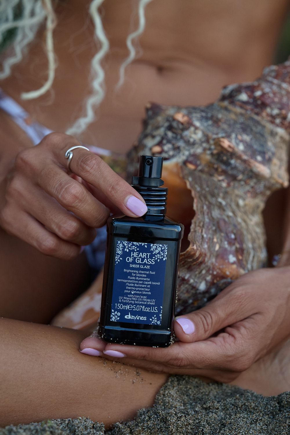 Hands with light pink manicure hold a black perfume bottle against a textured stone background.