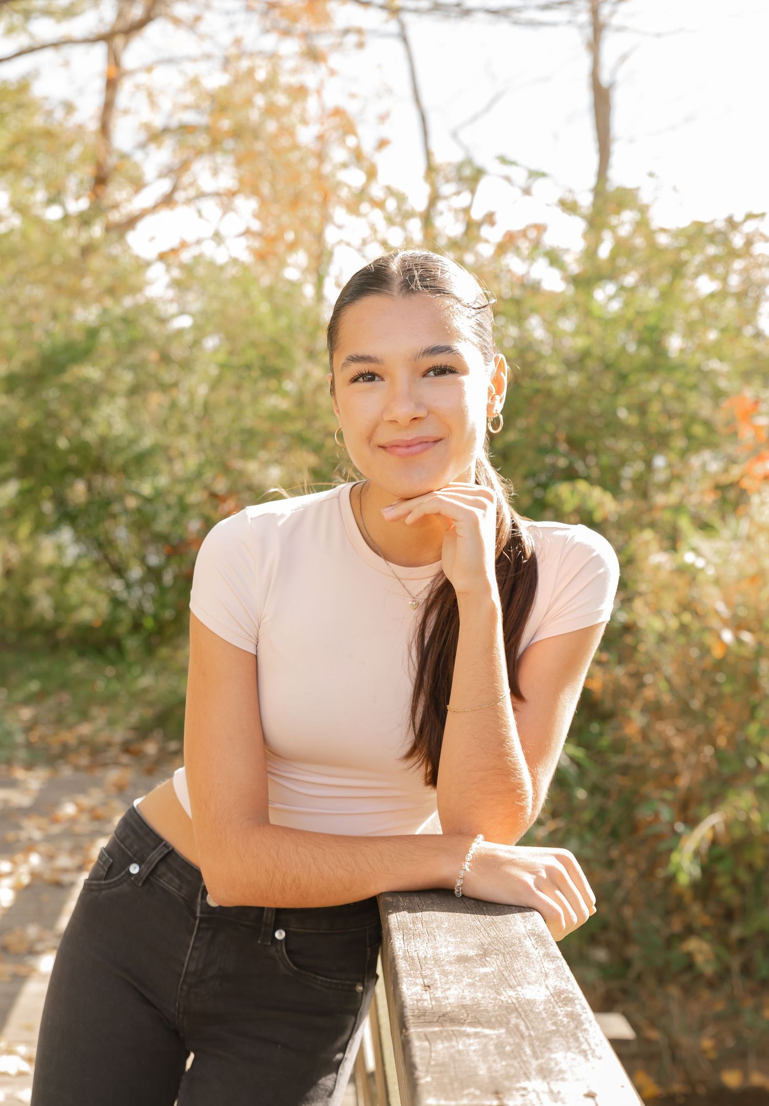 A casual outdoor portrait with someone in a cream top leaning on a wooden railing.