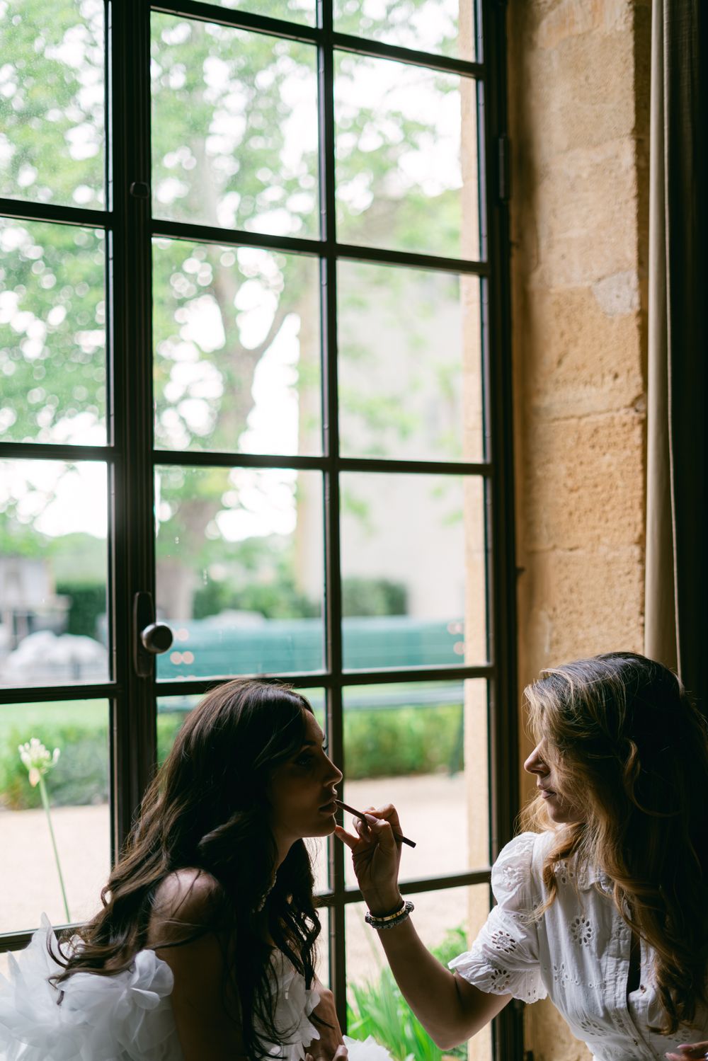Two figures preparing together by a sunlit window in casual white outfits.