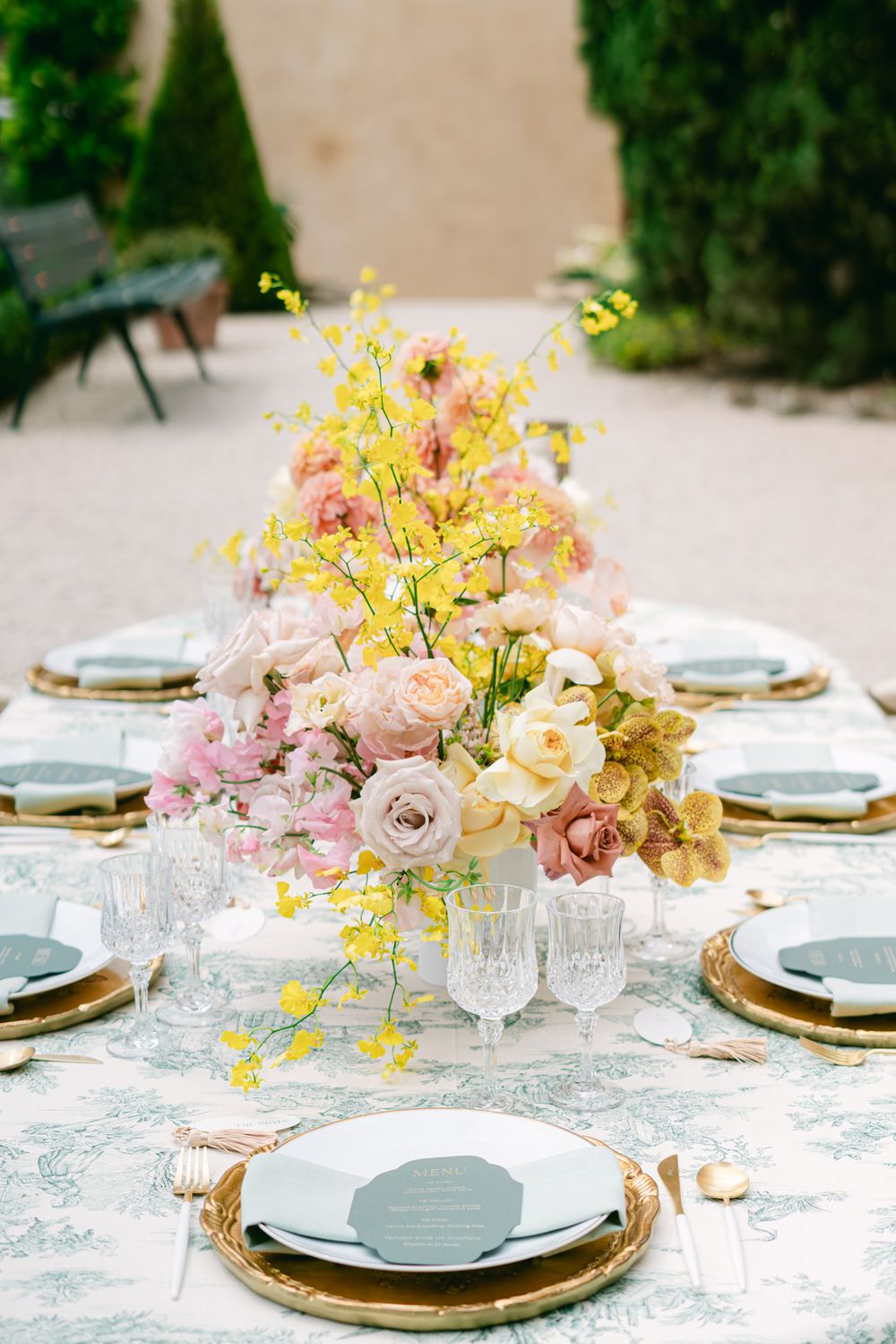 Luxurious table setting with pink and yellow floral centerpiece and gold charger plates.