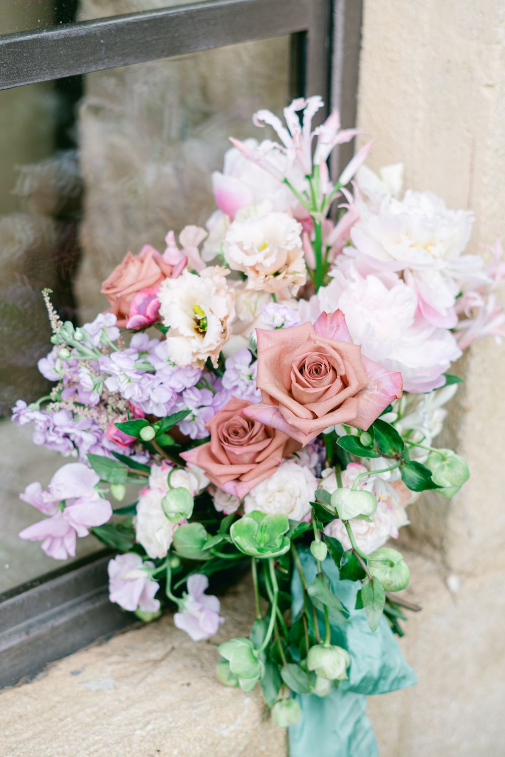 Romantic wedding bouquet featuring pink roses, white flowers, and purple accents in a soft pastel palette.