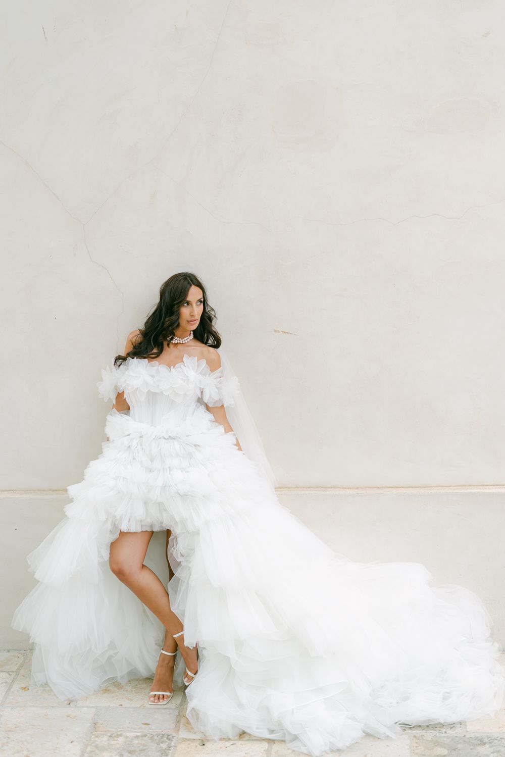 Dramatic bridal portrait against white wall with flowing tulle train.