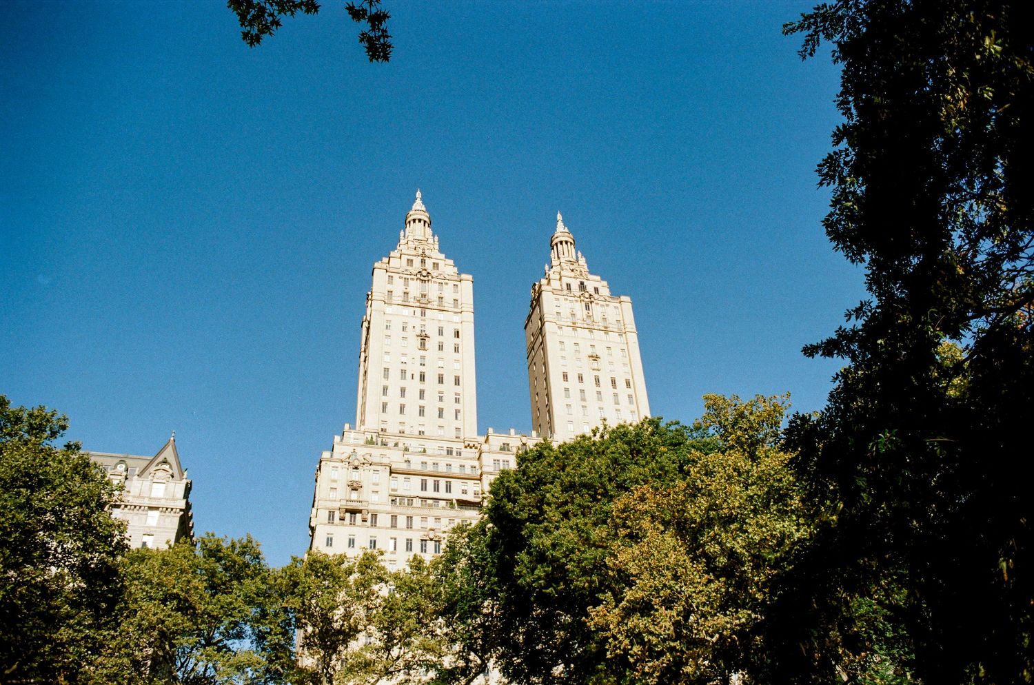 Twin towers of the San Remo building rising above Central Park trees against blue sky.