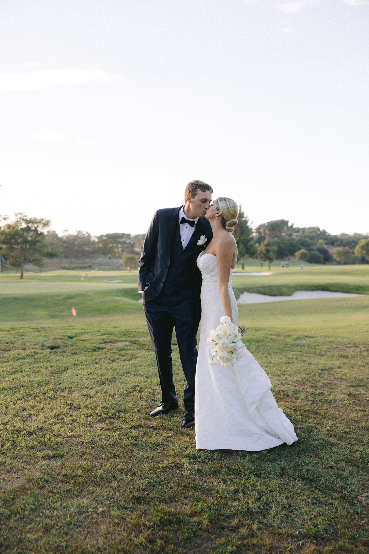 A bride and groom share a romantic moment together on a scenic golf course during golden hour.