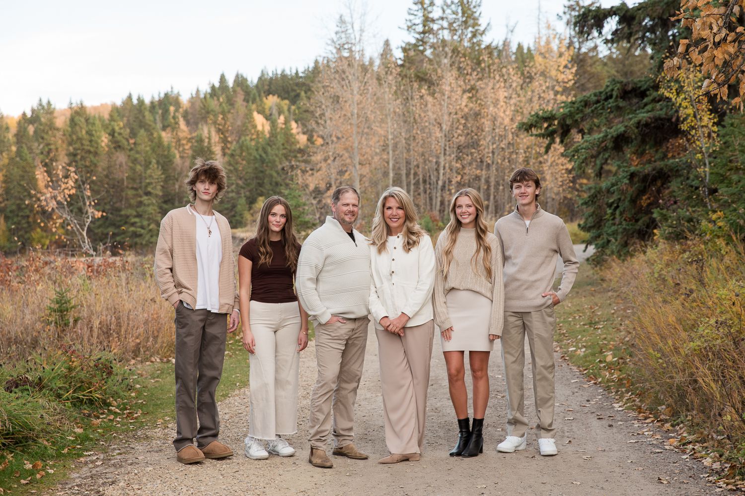 Group poses together on a forest path wearing coordinated neutral-colored outfits.