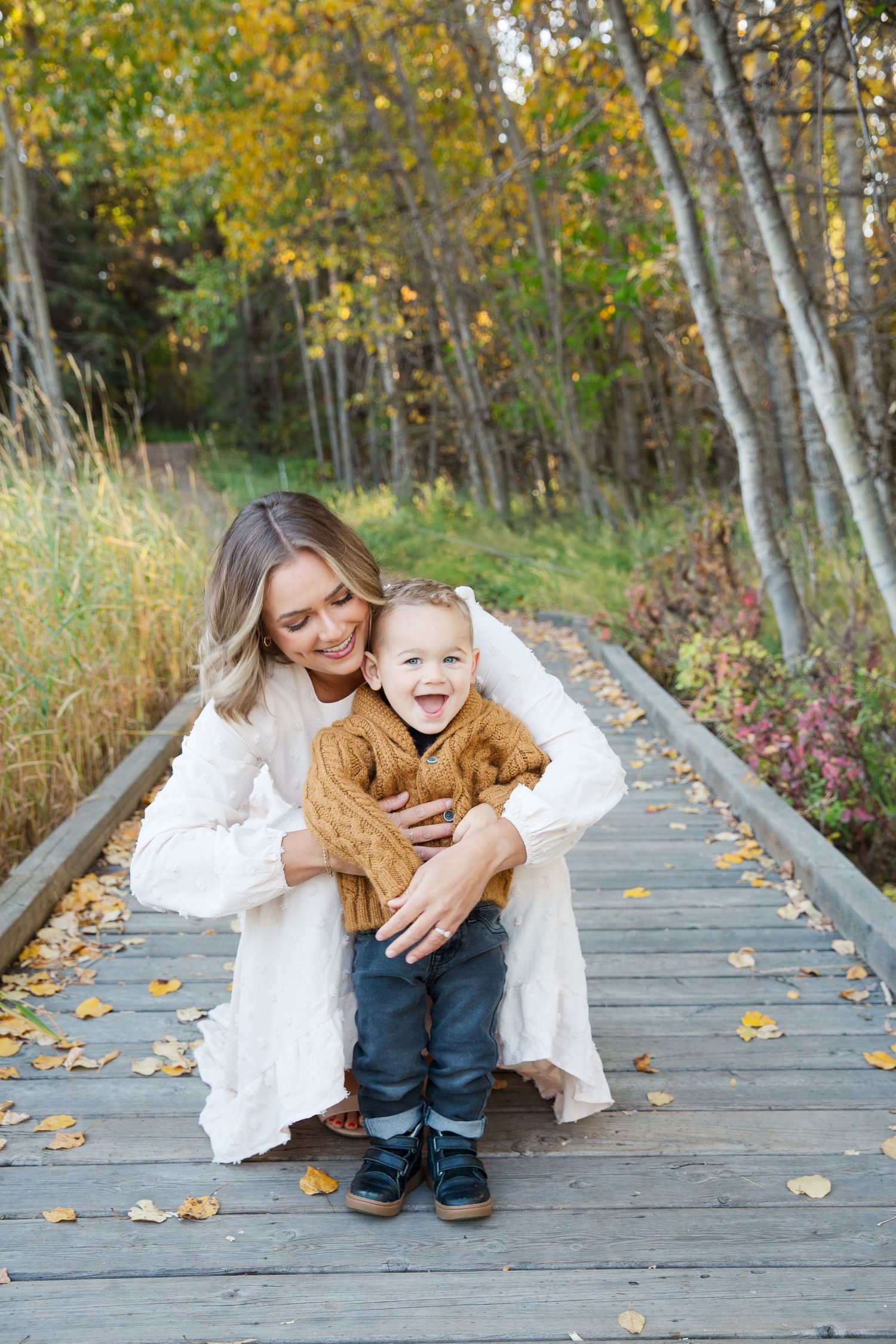 Autumn photo session on wooden boardwalk with yellow leaves and birch trees in background.