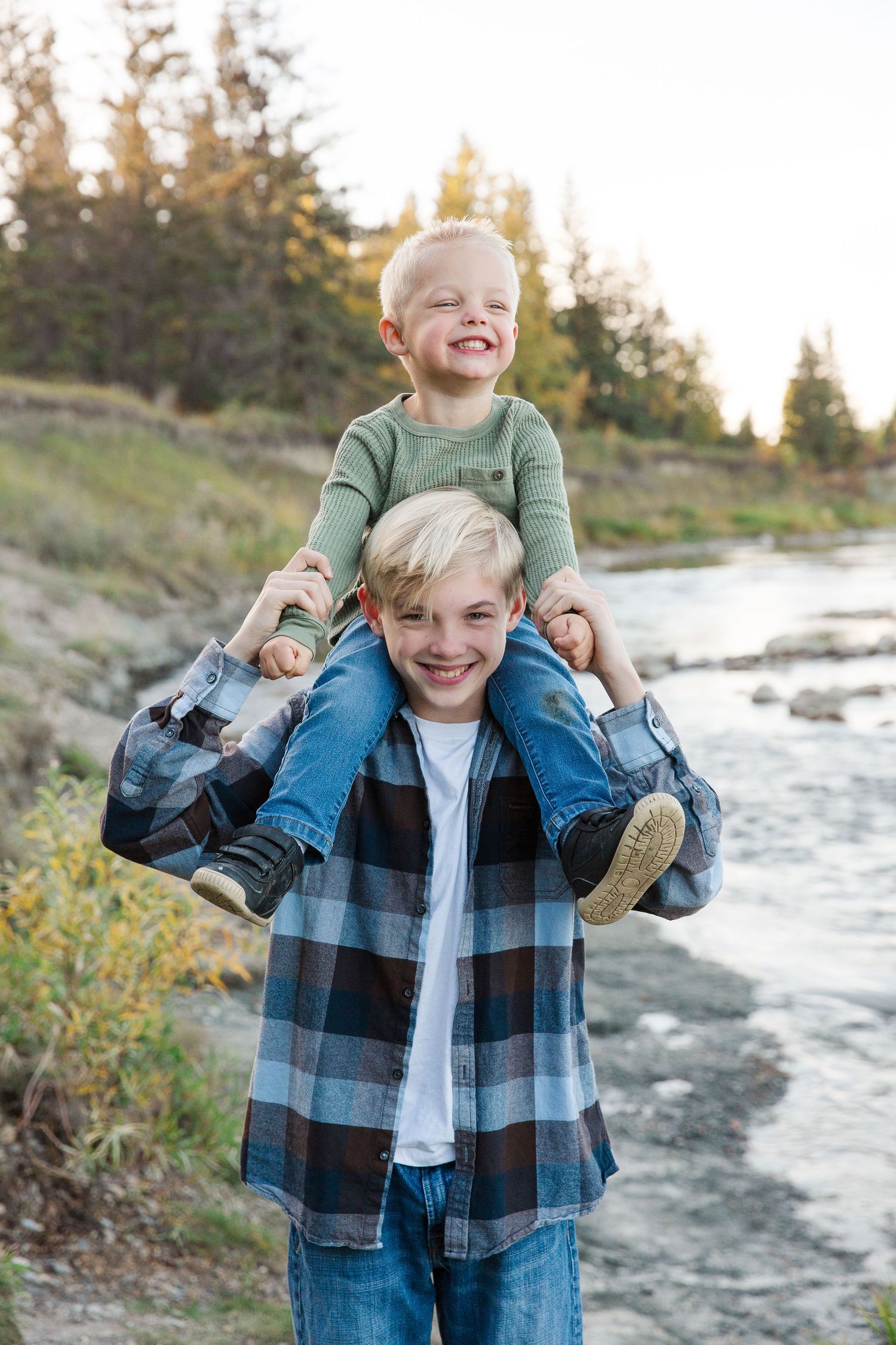 Playful siblings sharing a piggyback ride by riverside during golden hour.