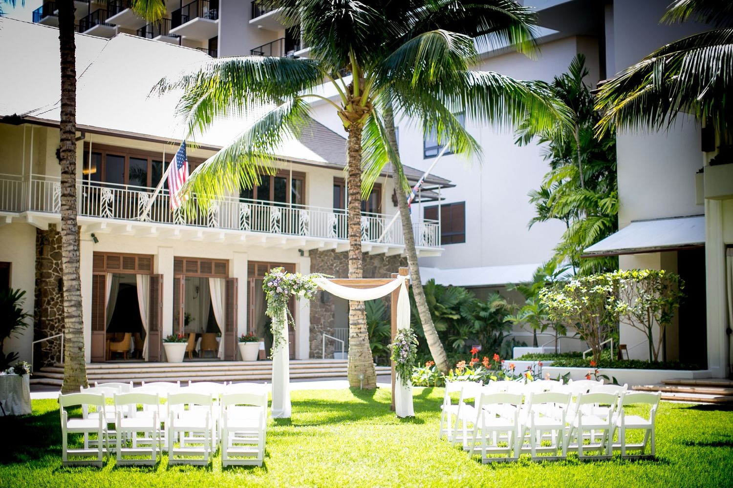 Outdoor wedding ceremony setup with white chairs on green lawn, palm trees, and elegant floral arch at Halekulani Hotel.
ハレクラニホテルウェディング
