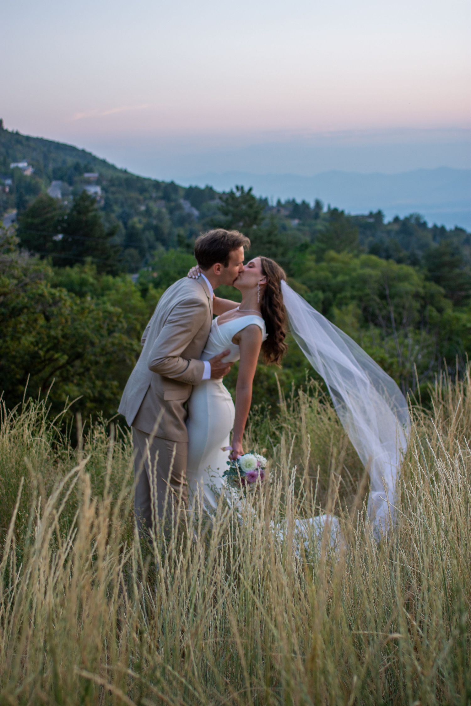 Bride and groom kiss in front of sunset on a Salt Lake City, Utah mountain.