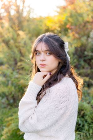 Portrait in cream knit sweater with warm autumn colors in background.
