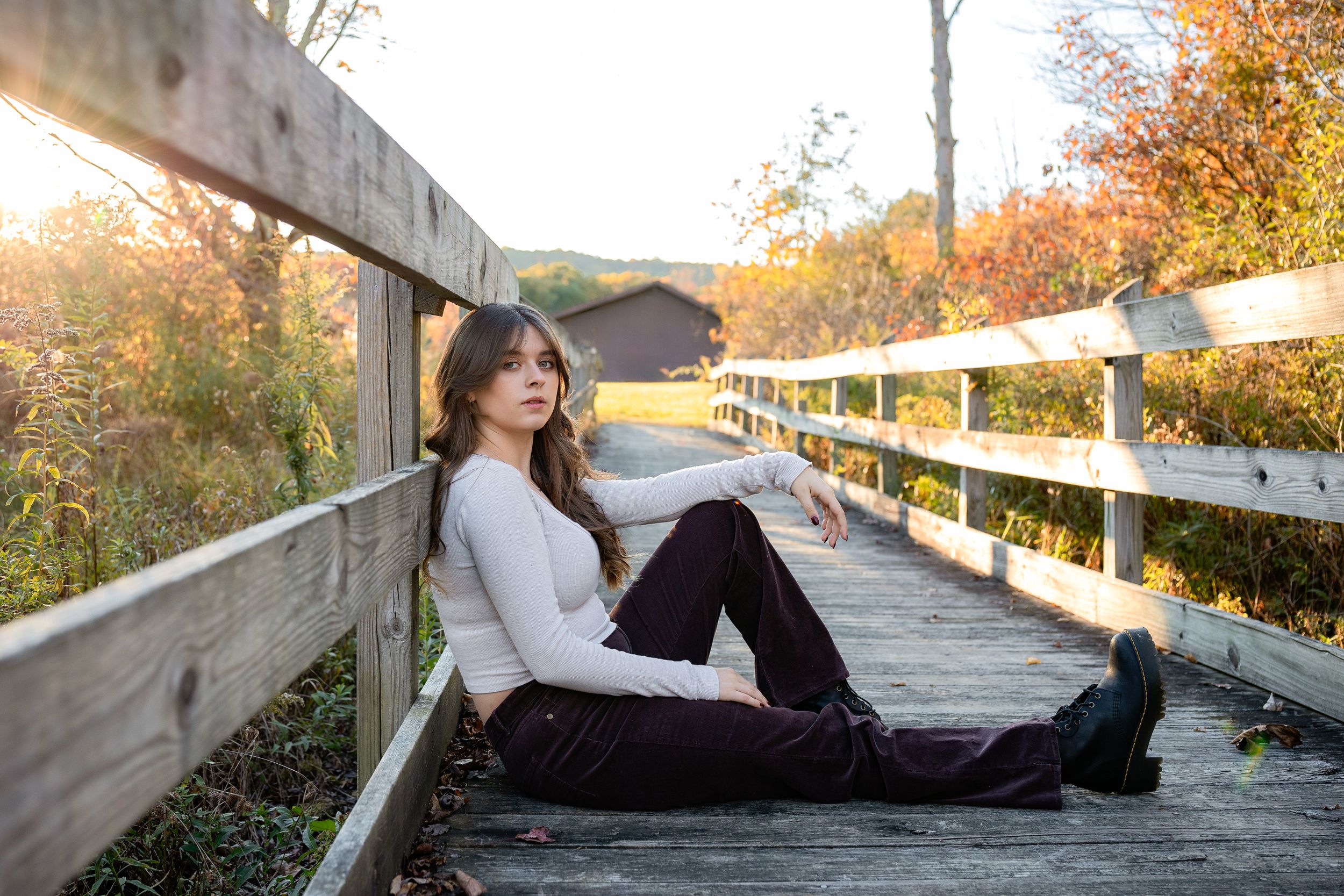 client relaxes on wooden boardwalk during autumn wearing white sweater and dark pants.