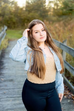 A client in denim jacket poses on wooden boardwalk during autumn sunset.