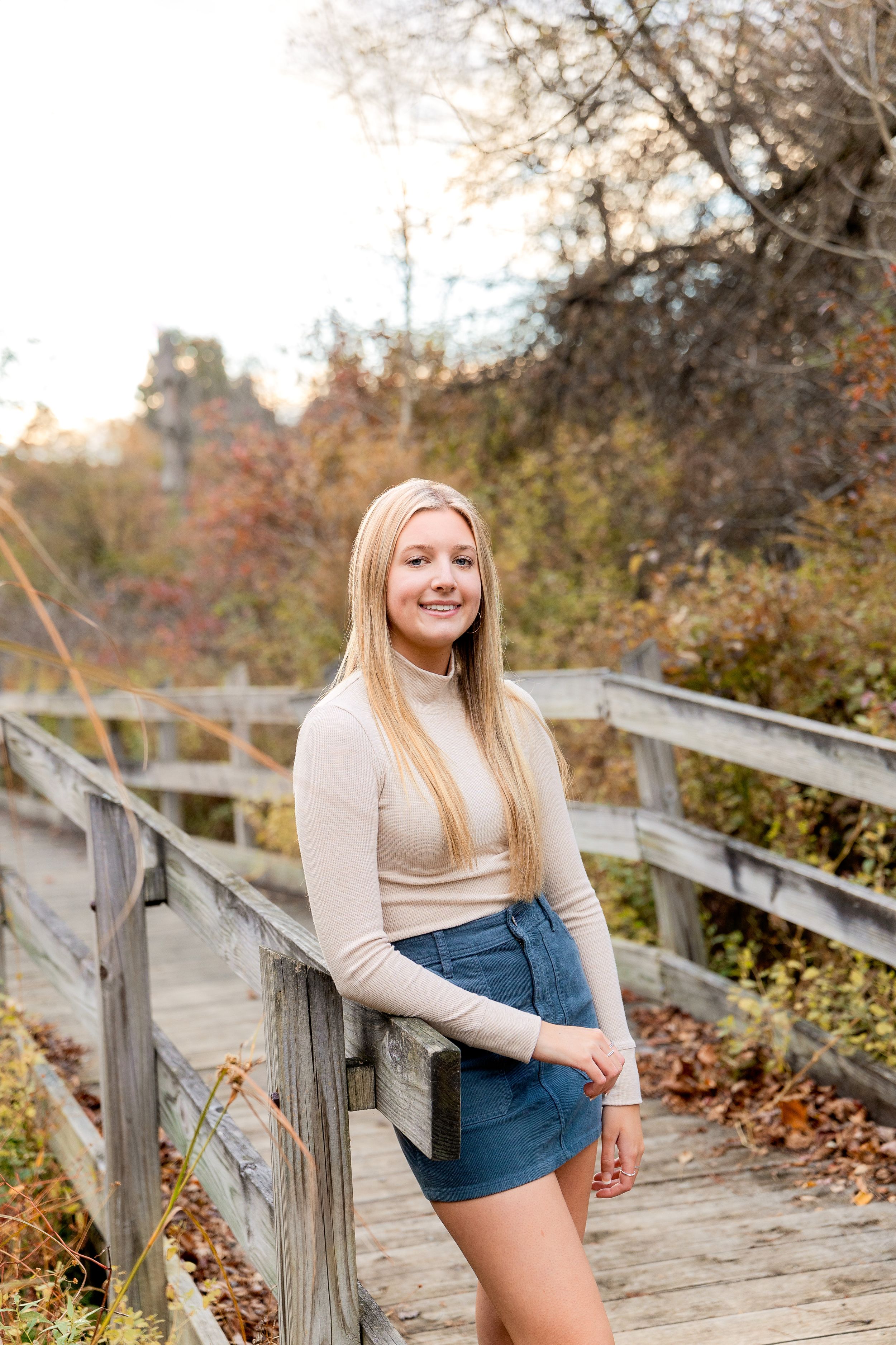A client in casual attire poses on a wooden boardwalk surrounded by autumn colors.