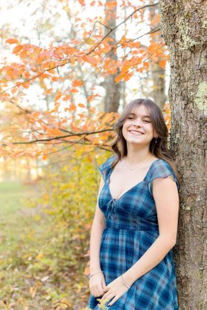 Fall portrait in plaid blue dress against backdrop of vibrant autumn leaves.