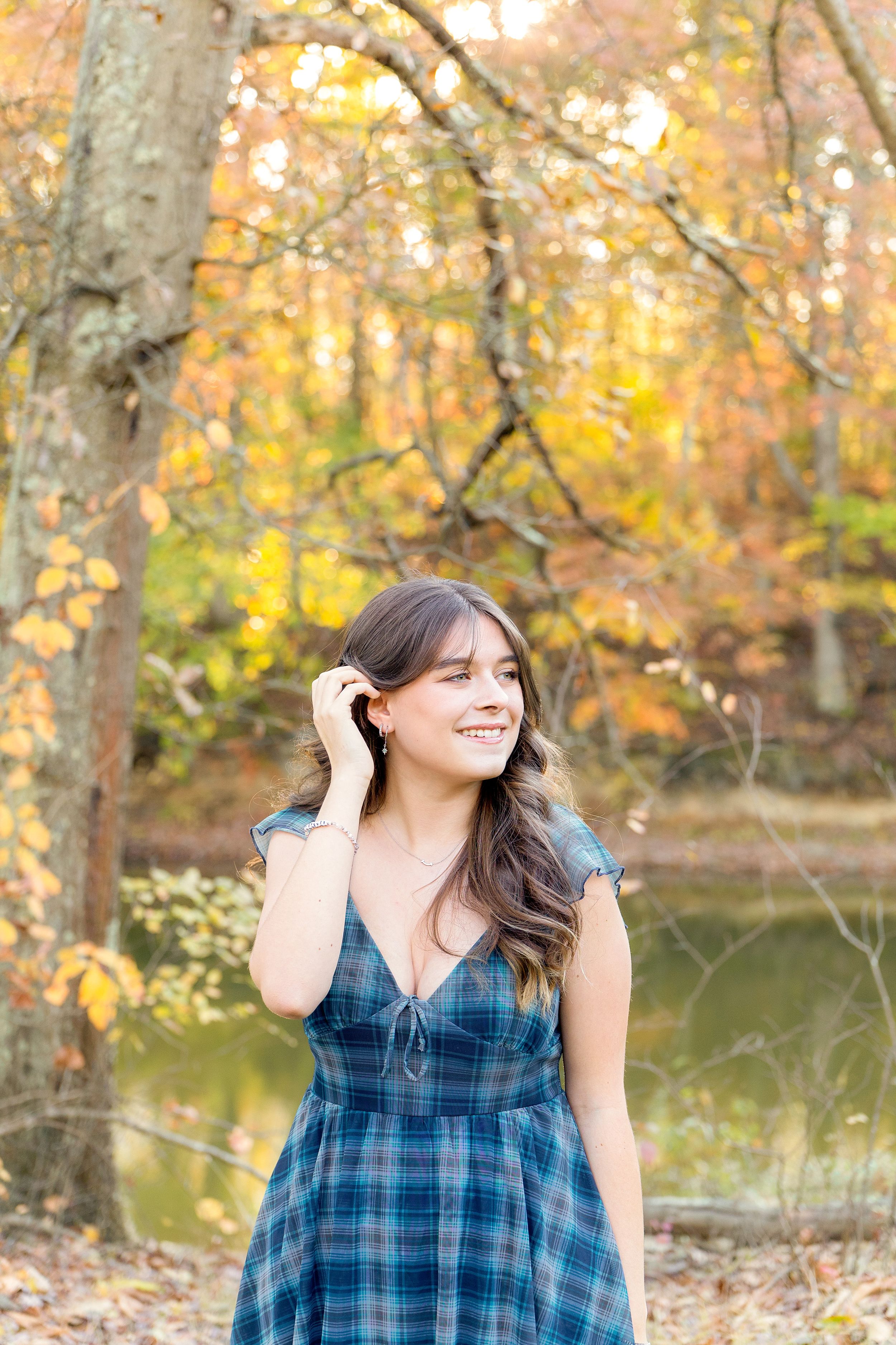 Autumn outdoor portrait in blue plaid dress with fall foliage and pond in background.