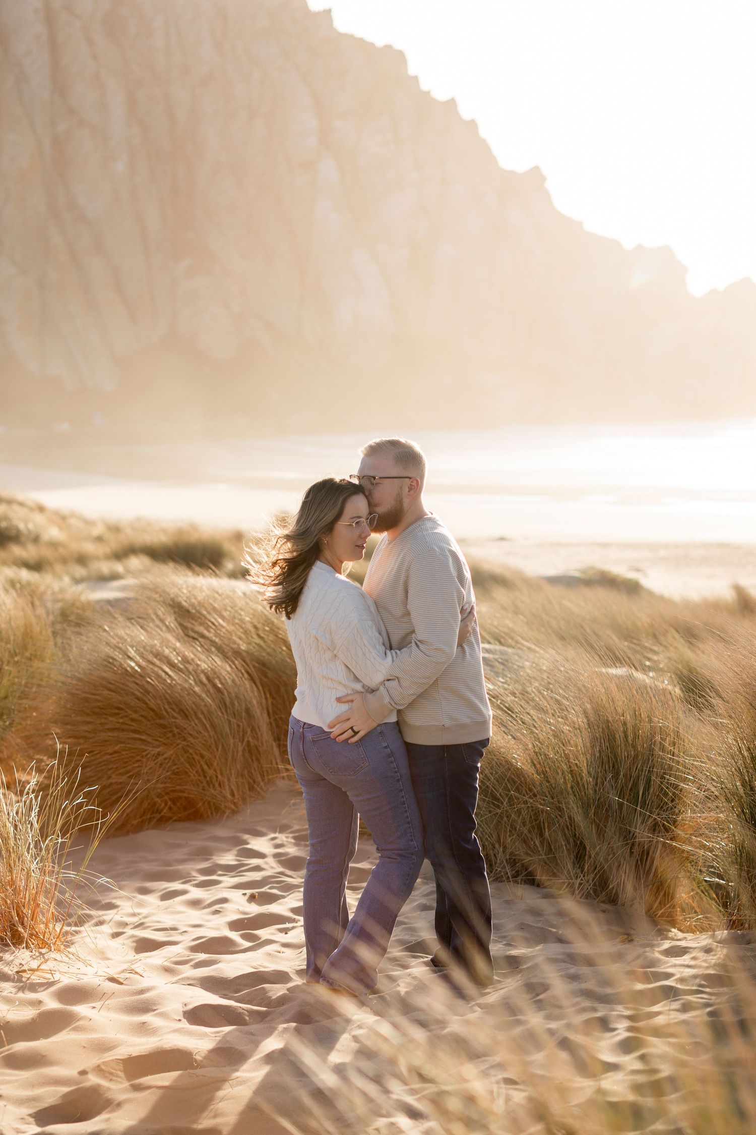 Romantic beach scene with couple embracing among sand dunes at golden hour.