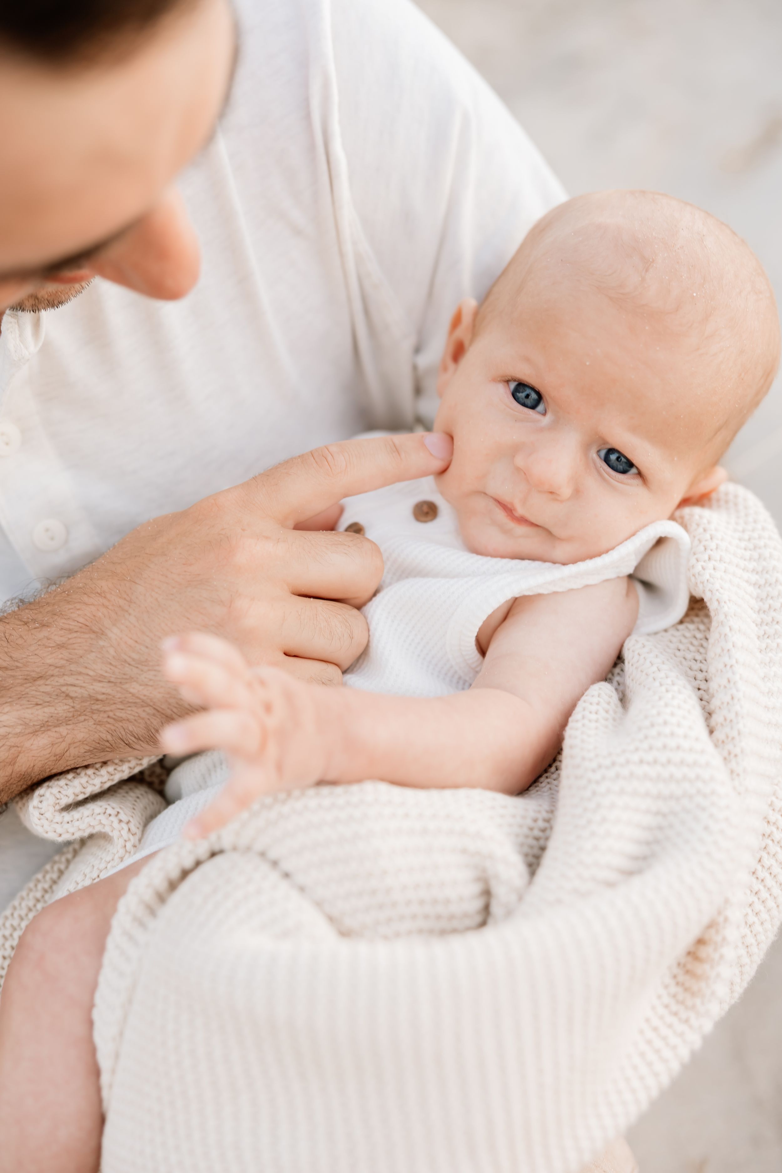 A baby swaddled in a soft white blanket being gently held and cradled by caring hands.