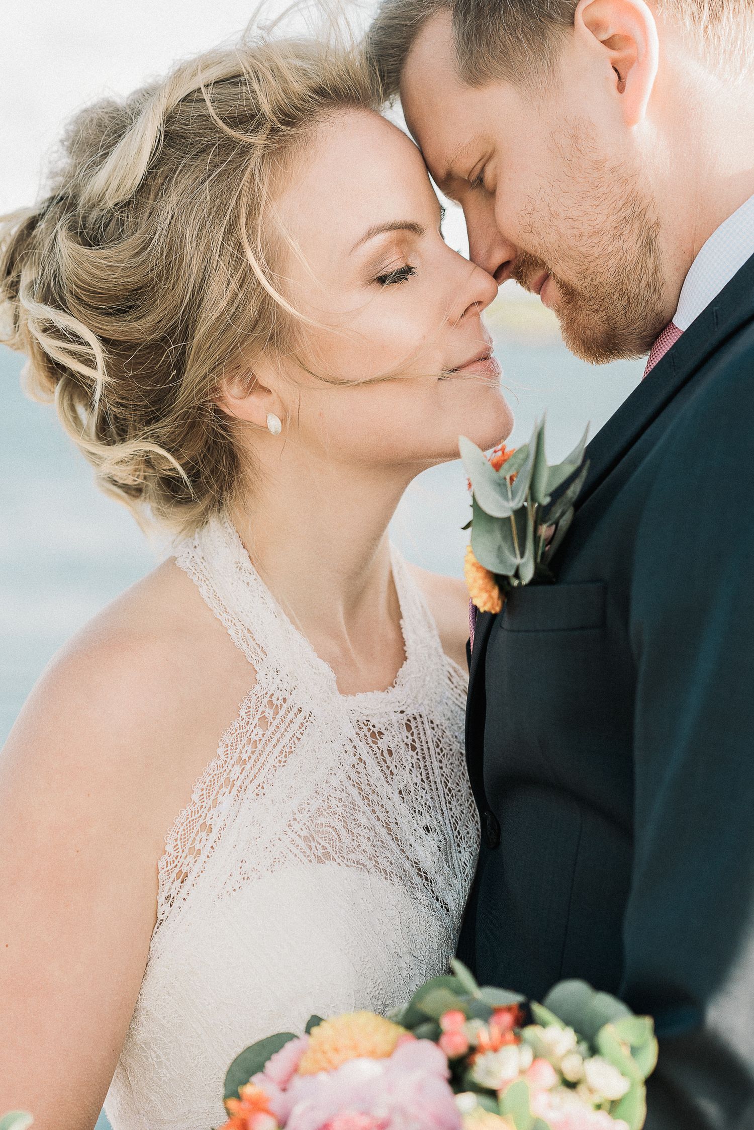 A romantic wedding portrait shows a bride in lace and groom in a black suit sharing an intimate moment together.