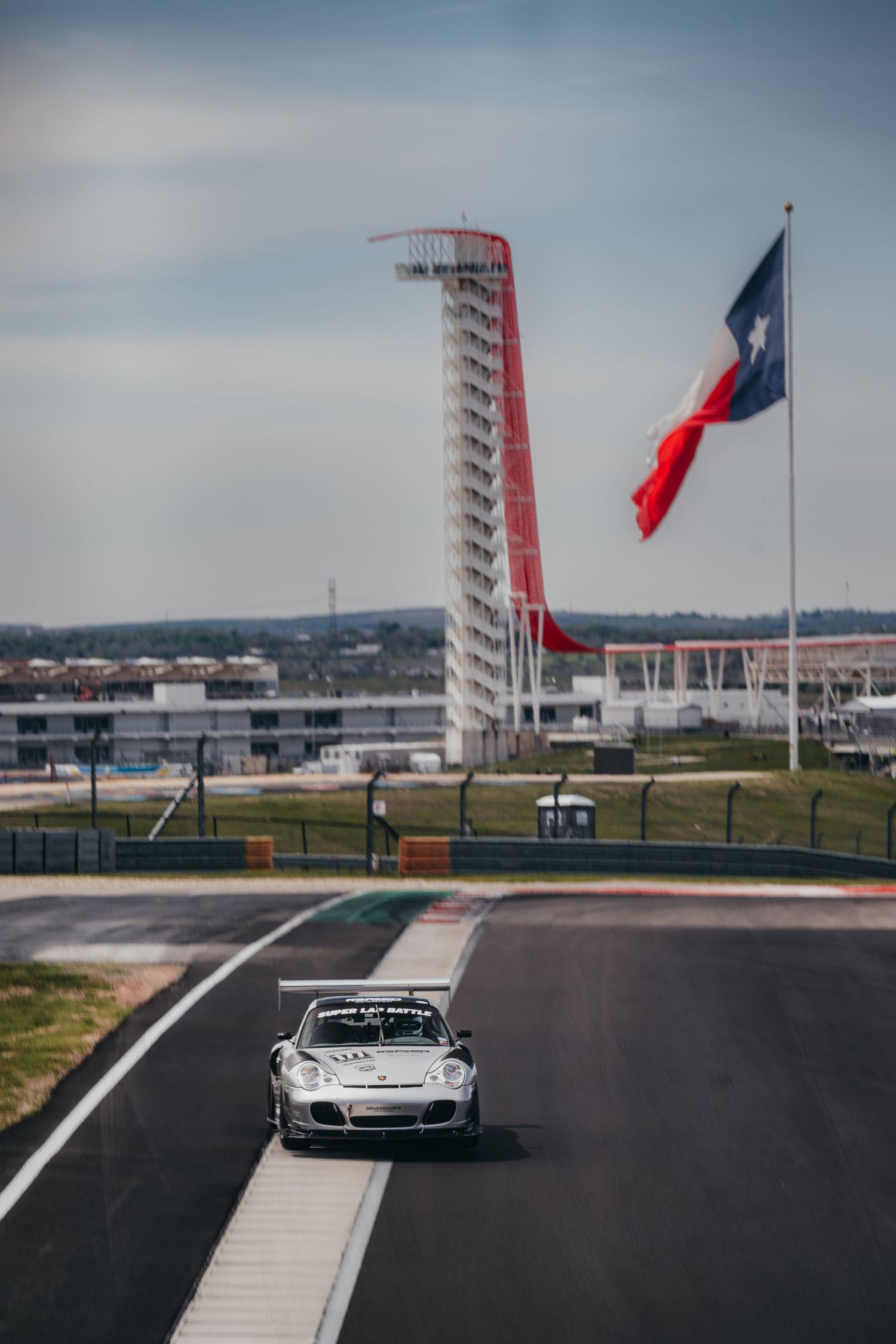 Race track with flagpoles and grandstands visible in the background on a cloudy day.