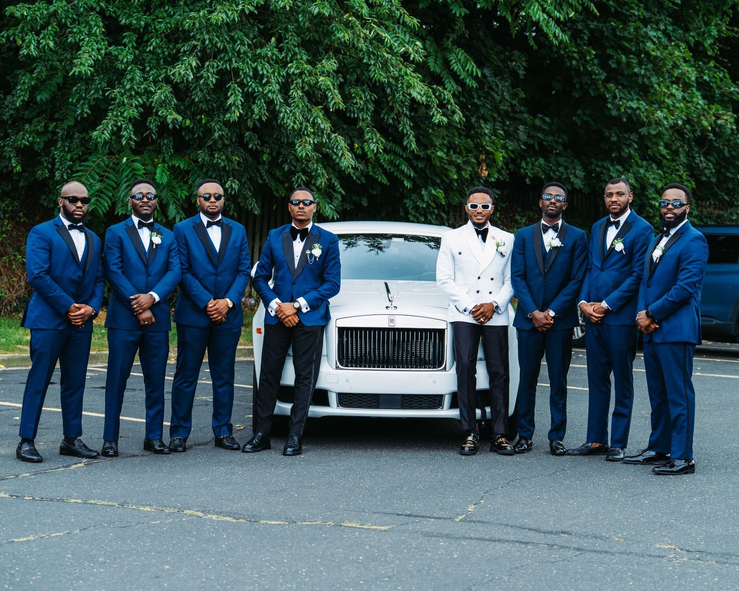 Wedding party in navy blue suits posing outdoors near white limousines.