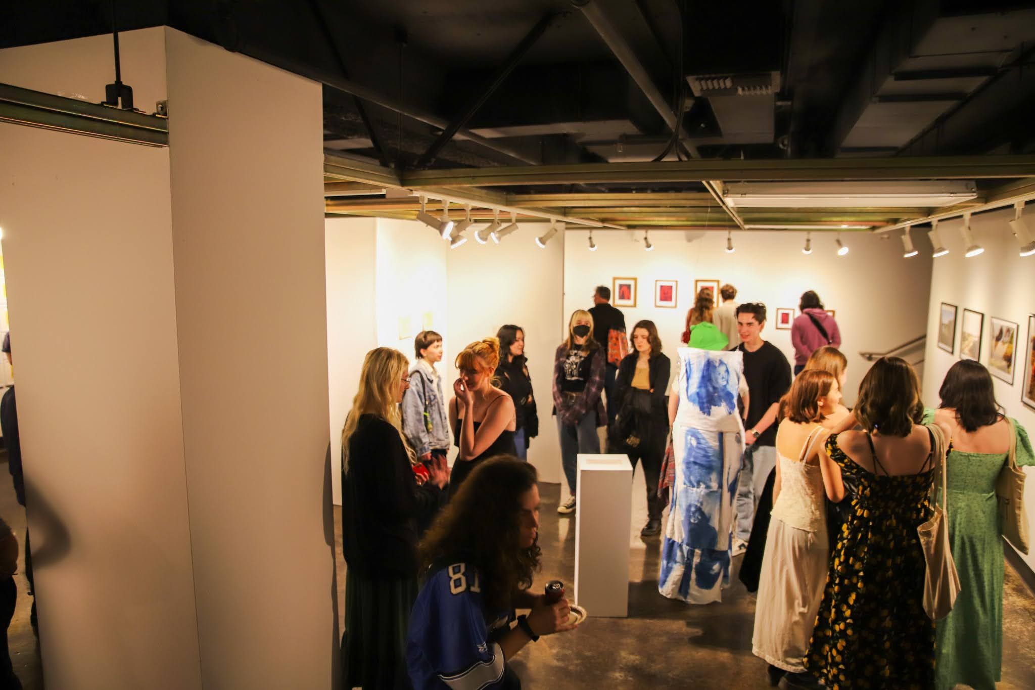 People viewing artwork displays in a modern gallery with white walls and track lighting.