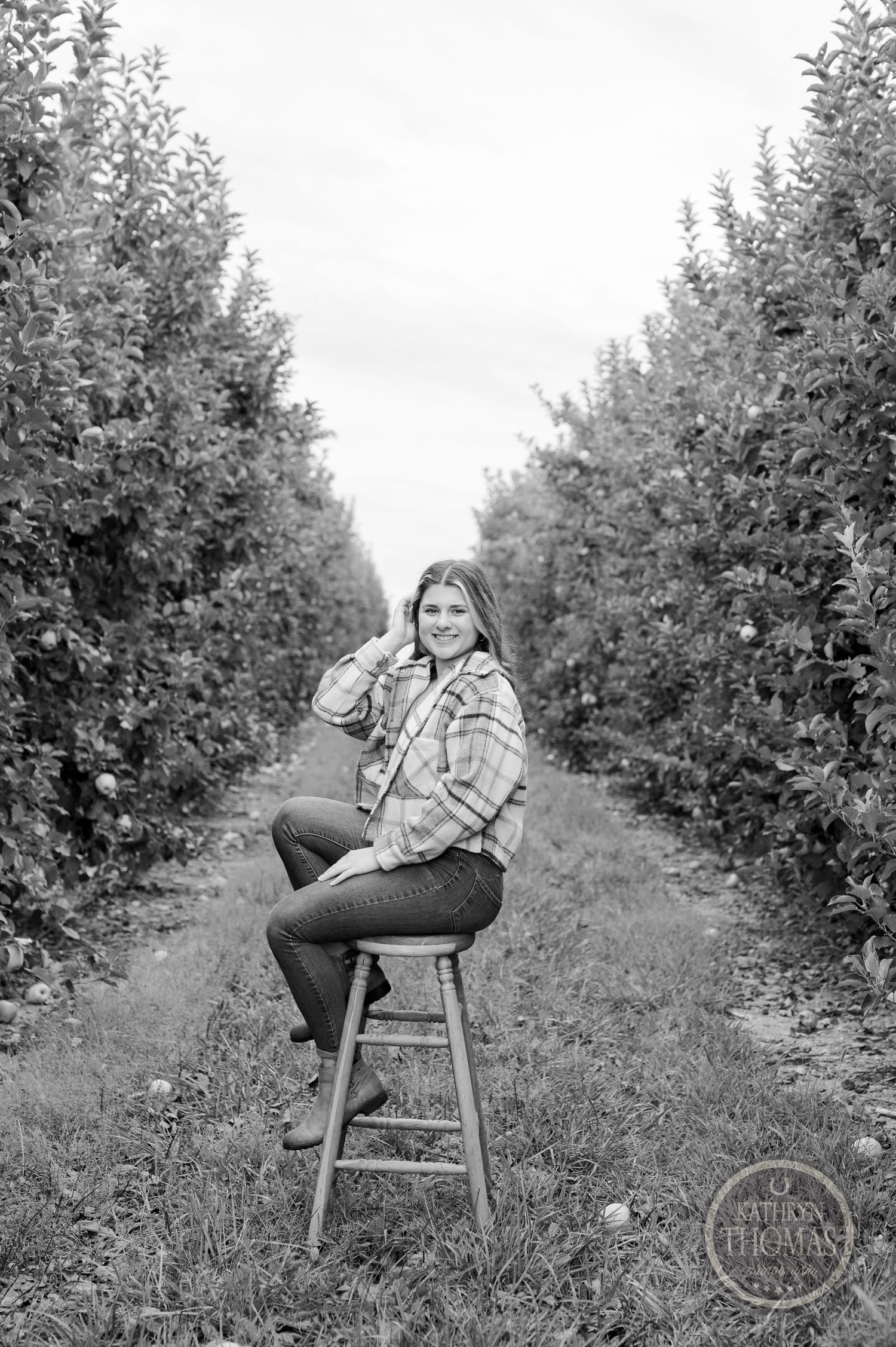 Black and white portrait of a person seated on a stool between rows of fruit trees in an orchard.