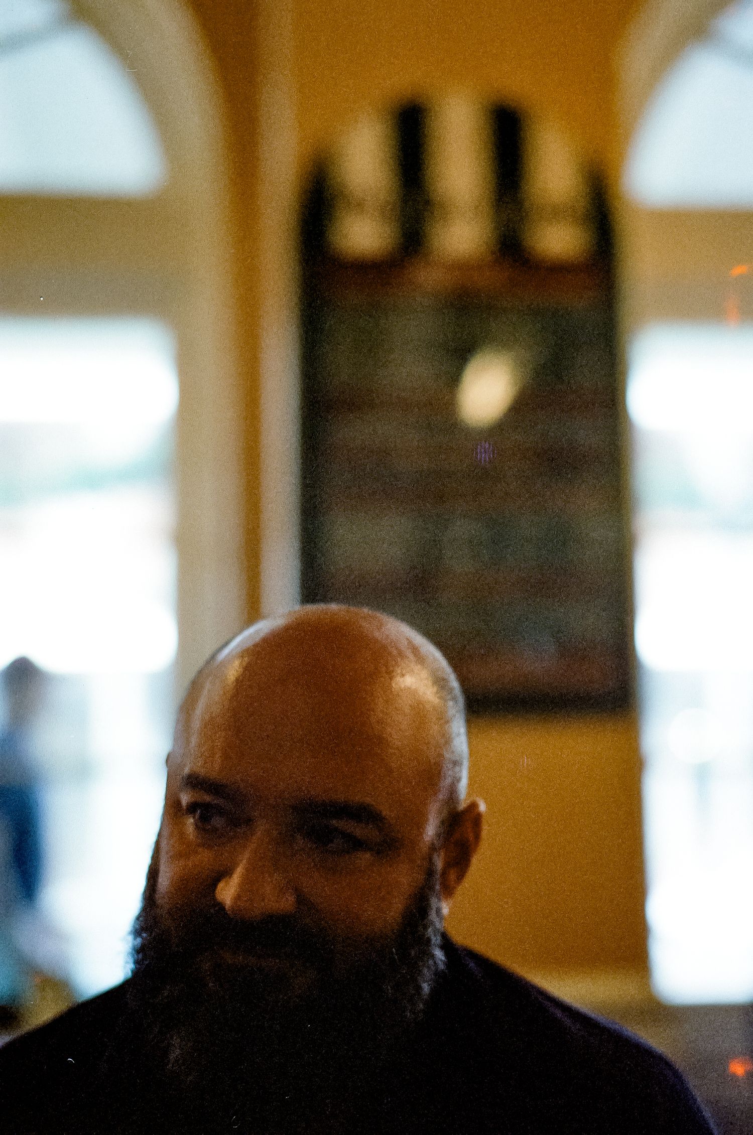 A person with a dark beard in warm indoor lighting with a blurred background.