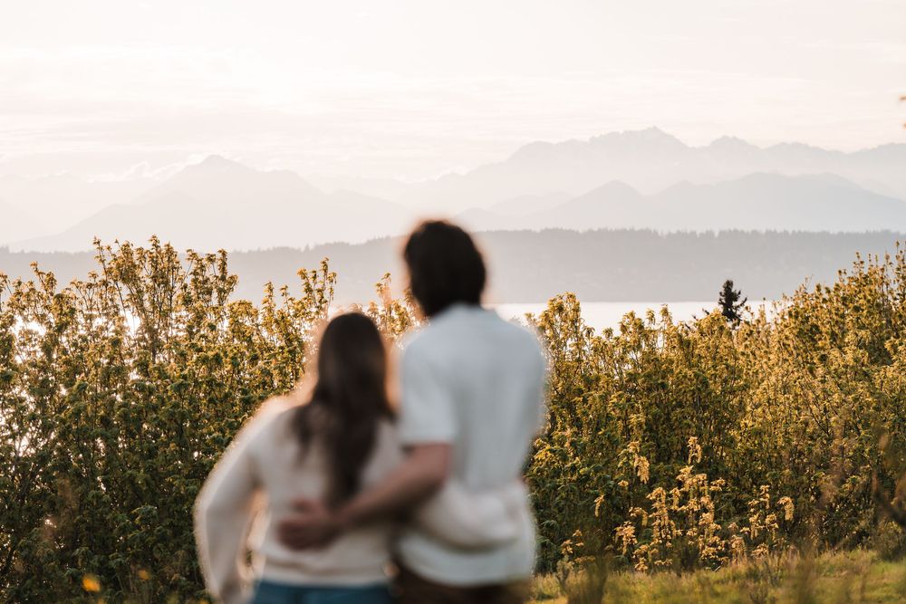 Couple standing together arm in arm overlooking a scenic mountain and water landscape at golden hour.