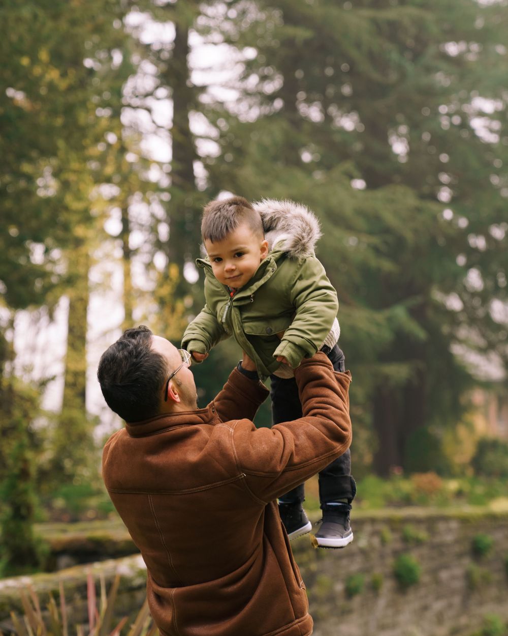 A joyful moment between parent and child playing outdoors among evergreen trees.