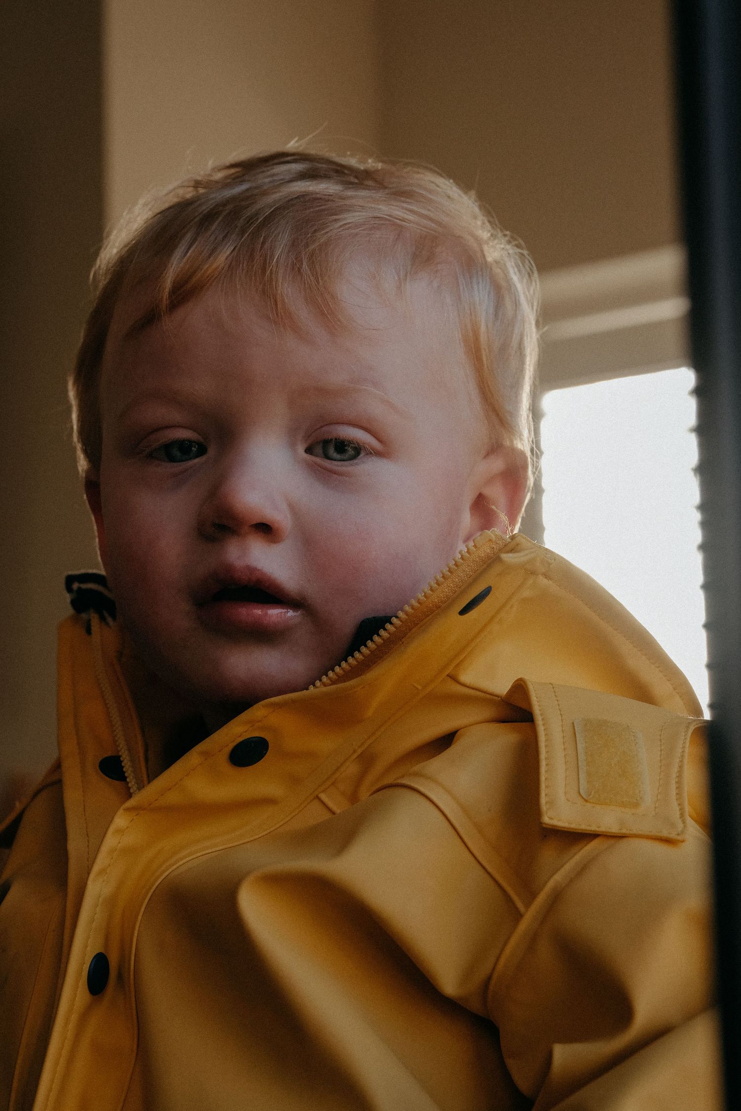 A young child wearing a bright yellow raincoat smiles at the camera in warm indoor lighting.