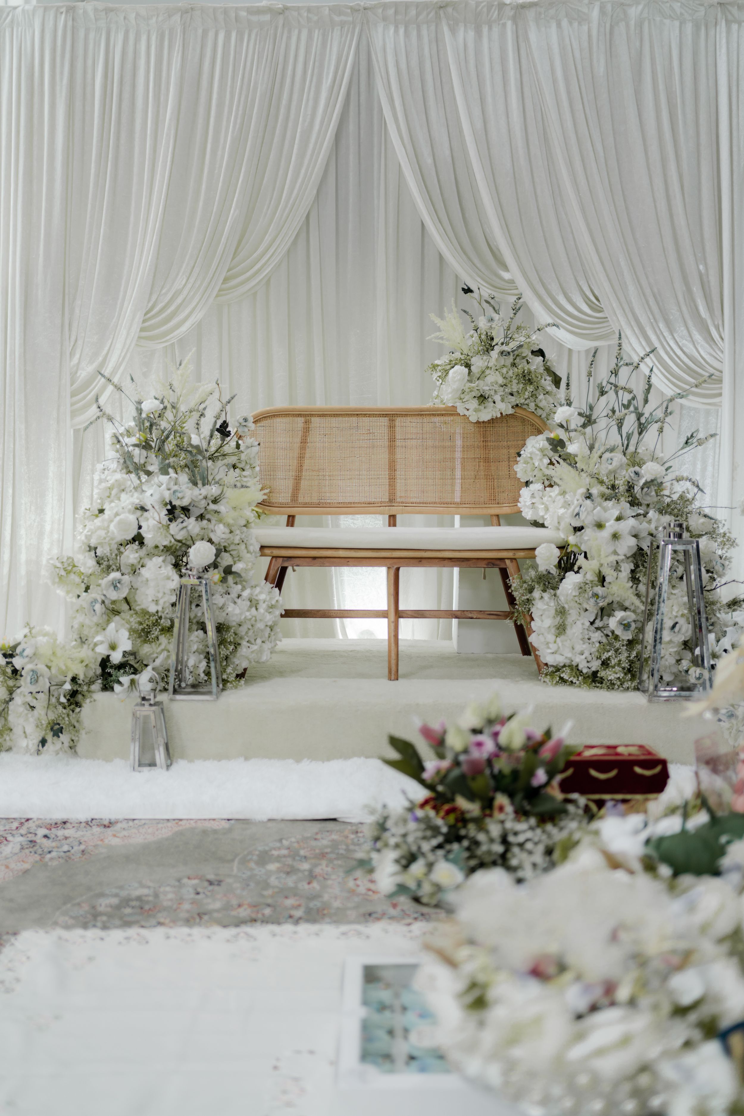 An elegant white wedding stage setup with flowing curtains and floral arrangements.