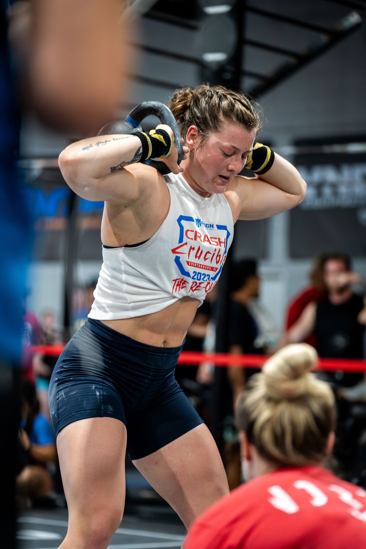 CrossFit athlete performs overhead kettlebell movement during competition.