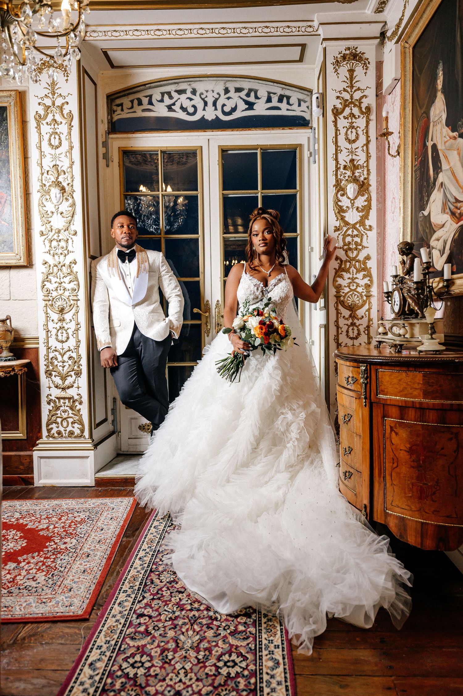 A wedding couple poses in an ornately decorated classical interior with gilded details.