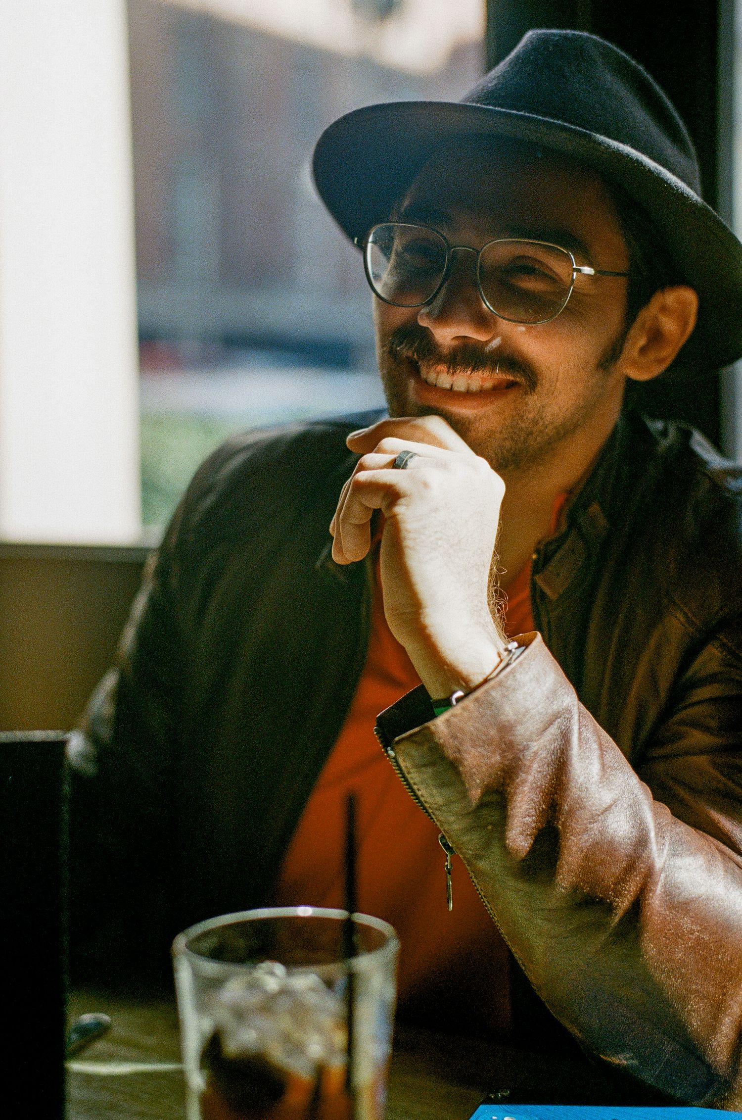 A patron in a black hat and glasses smiles while relaxing at a casual dining establishment.