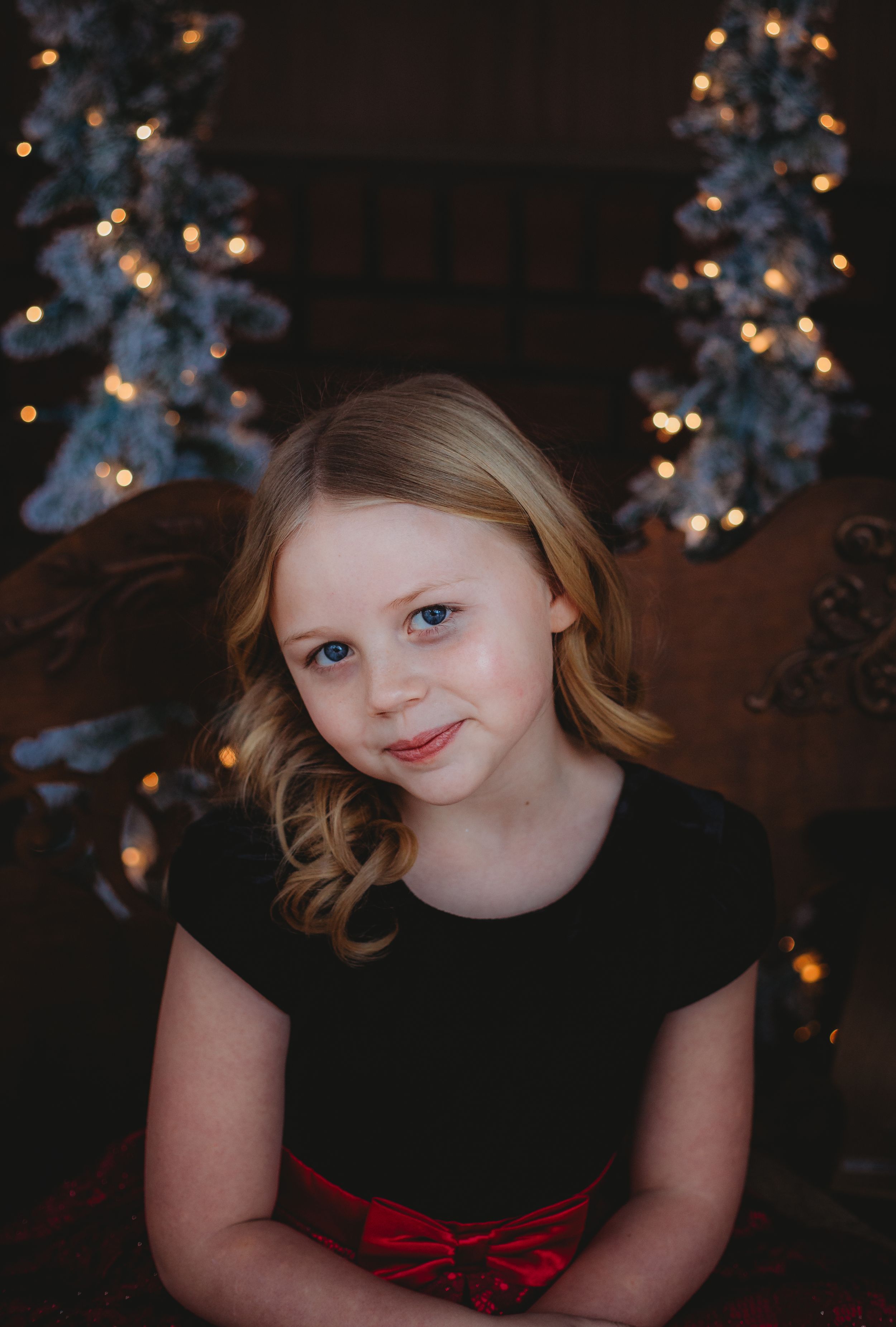 A holiday portrait with Christmas trees and twinkle lights in the background.