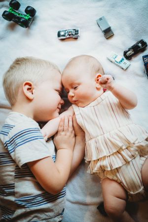 Two young siblings lying together with toy cars scattered around them.