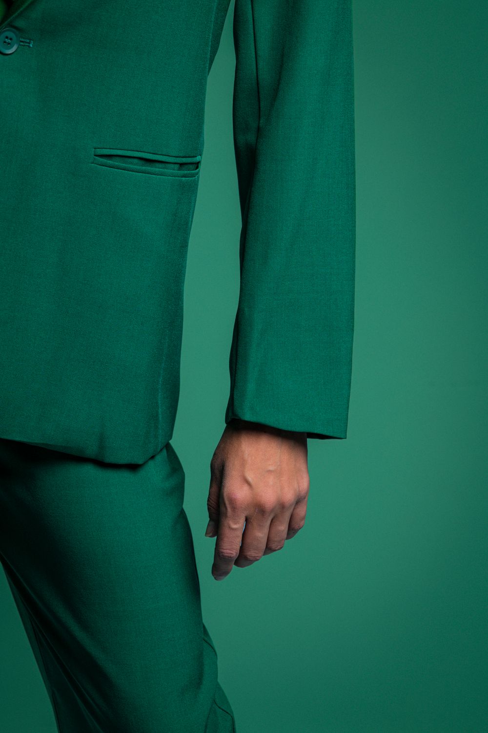 Close-up of emerald green suit sleeve and hand against matching green background.