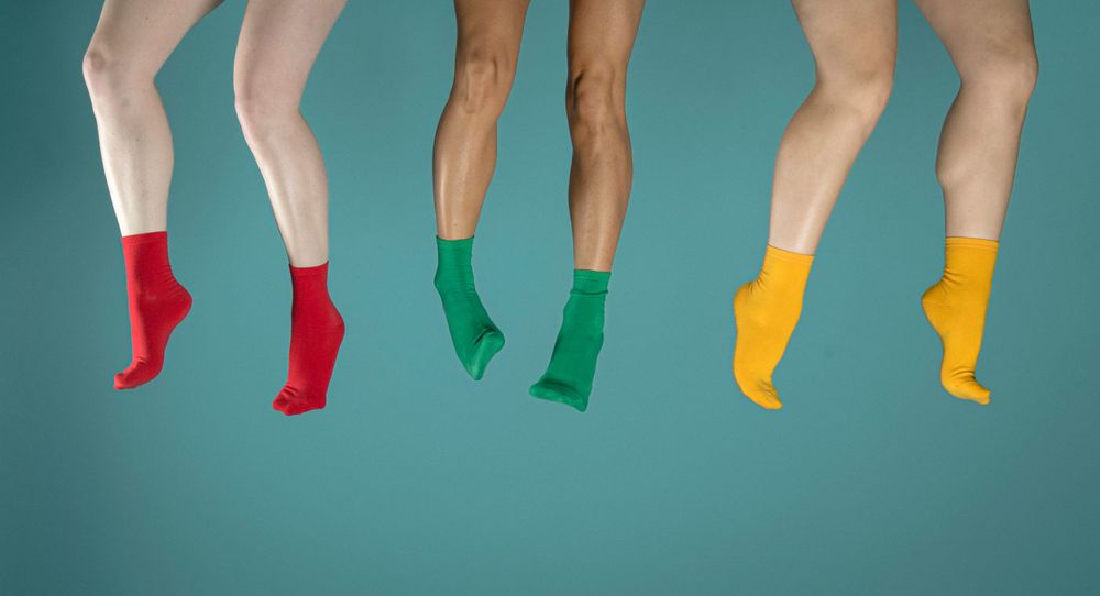 Legs wearing colorful socks in red, green, and yellow jumping against turquoise background.