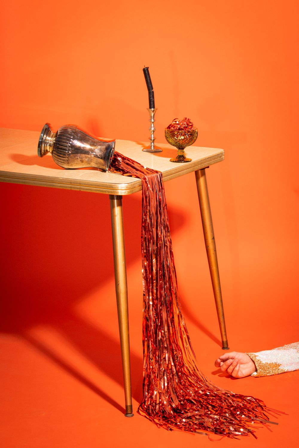 Still life with overturned glass trophy spilling red chains on wooden table against orange background.