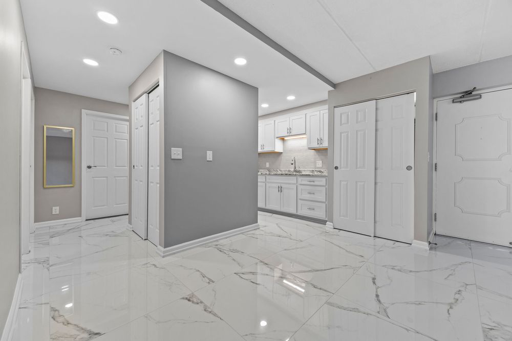 Bright basement with white marble tile floors, gray walls, white cabinetry, recessed lighting, and multiple doors.
