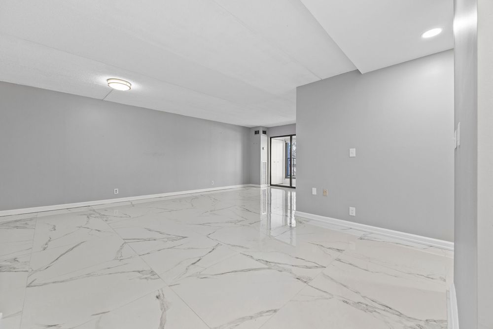 Spacious empty room with glossy white marble floors and light gray walls in a modern residential space.