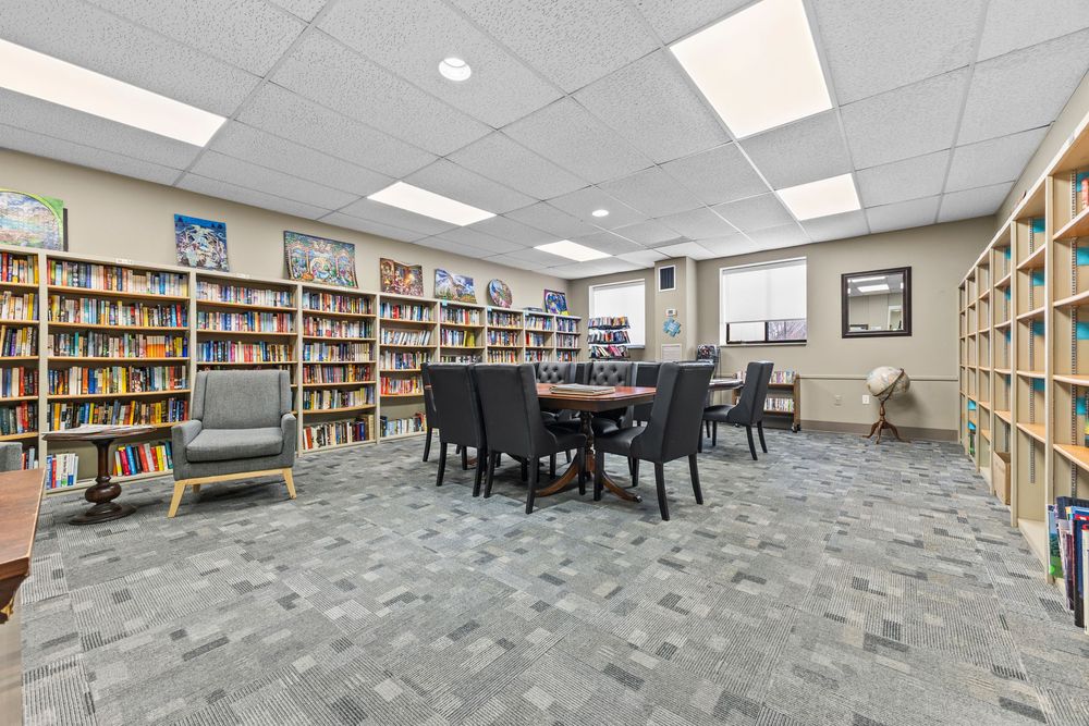Community library and meeting room with floor-to-ceiling bookshelves and central dining table.