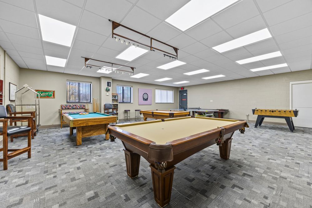 Recreation room featuring two pool tables, foosball, and bright drop ceiling lighting.