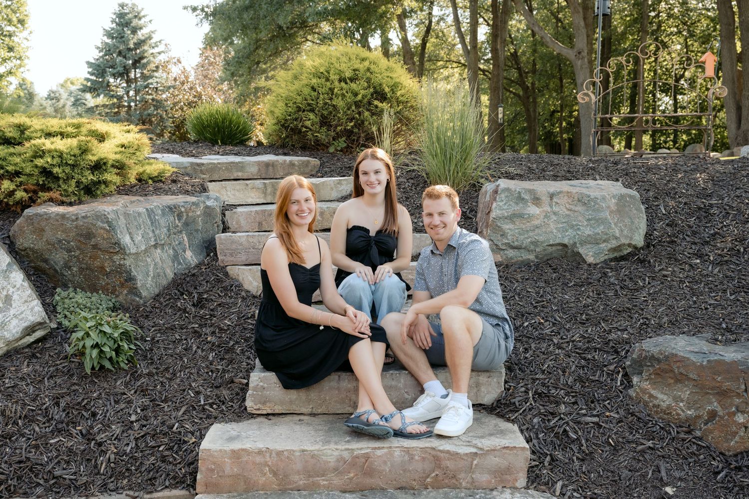 three teenage siblings sit on stone steps for posed family portrait at the cabin on lake wissota in chippewa falls