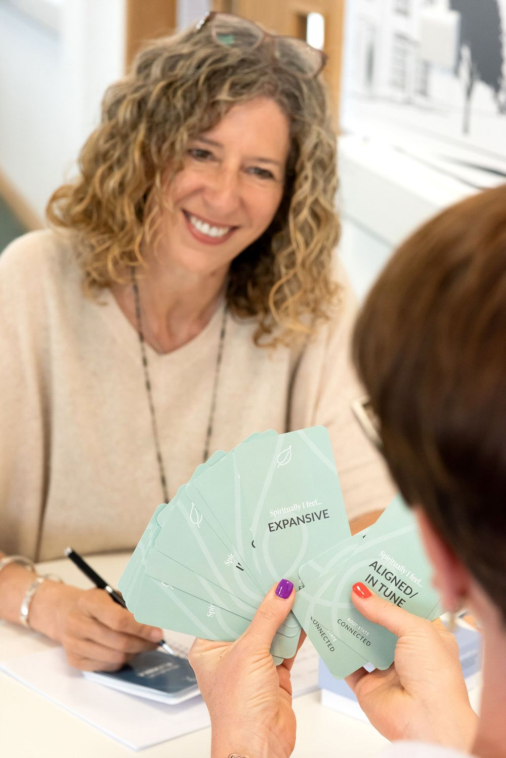 A person with curly hair smiles while holding and reviewing mint-colored documents at a table.