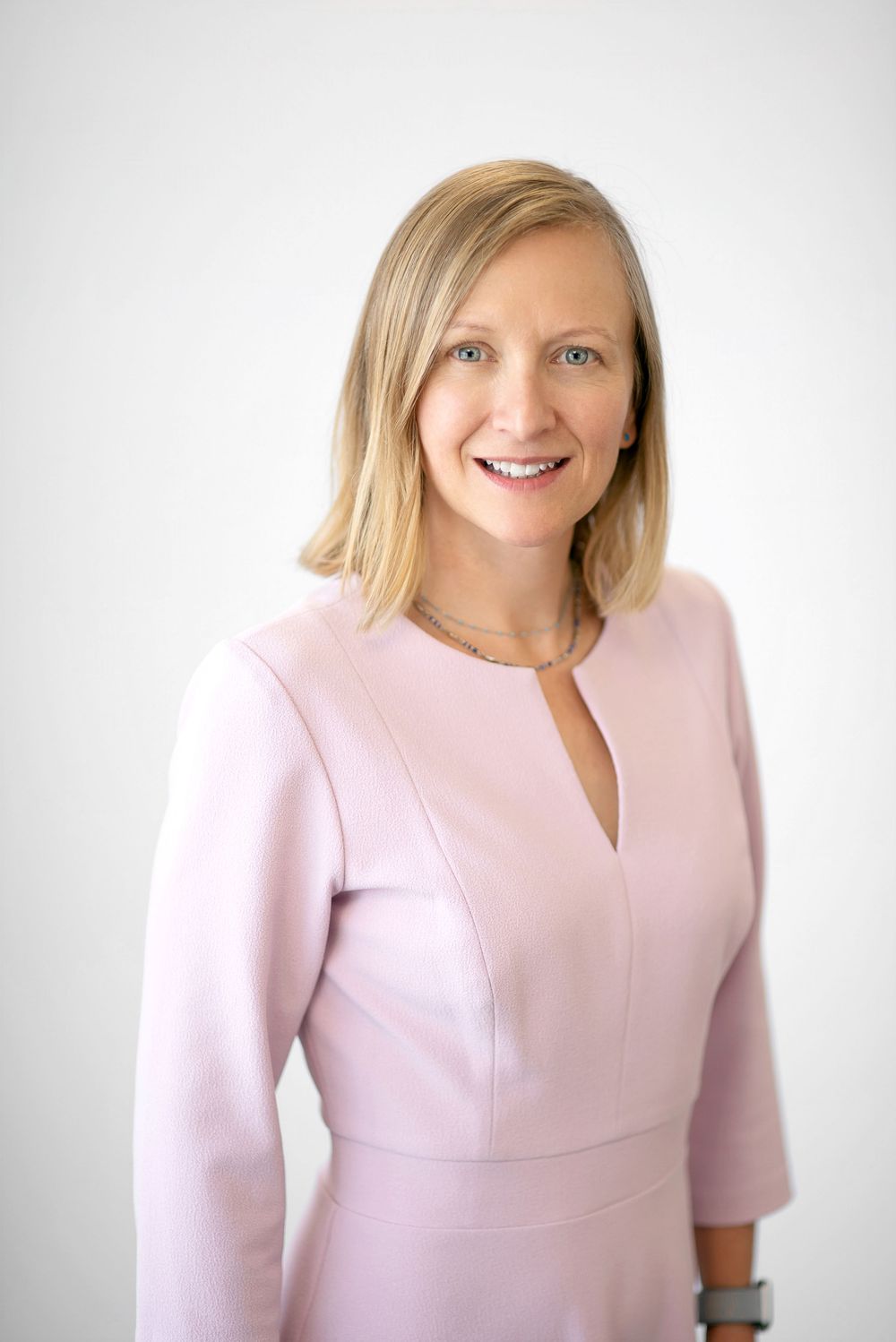 Professional headshot of someone wearing a light pink dress against a white background.